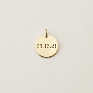 May include: A circular gold-toned metal pendant featuring a small jump ring at the top for attachment. The front surface of the smooth, polished disc is engraved with the date 03.13.21 in a clean, dark, serif font centred on the metal face.