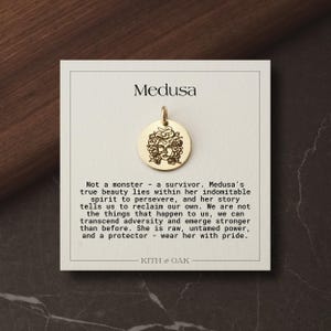 Könnte beinhalten: Ein goldfarbener runder Anhänger mit einer eingravierten Strichzeichnung von Medusa. Der Anhänger ist auf einer quadratischen weißen Karte befestigt, die oben den Text Medusa und einen Text über eine Überlebende enthält, gefolgt von KITH & OAK.