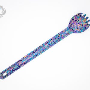May include: A blue, purple, and yellow patterned stainless steel spoon with a fork on the end.