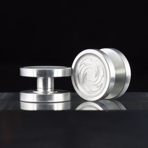 May include: Two silver metal fidget spinners. One spinner has a swirling design on the top. The other spinner is plain.