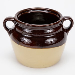 May include: A brown and beige ceramic crock with two handles. The crock has a glazed finish and is perfect for storing food.