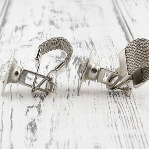 May include: A pair of silver cufflinks with a clear crystal stone on one and a silver mesh design on the other.