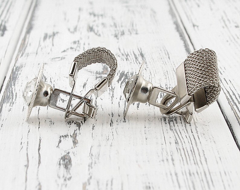 May include: A pair of silver cufflinks with a clear crystal stone on one and a silver mesh design on the other.