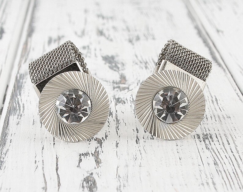 May include: A pair of silver cufflinks with a mesh design and a clear rhinestone in the center of each cufflink.