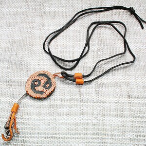 May include: A black leather cord necklace with a round pendant. The pendant is made of orange and black leather and has a swirling design.