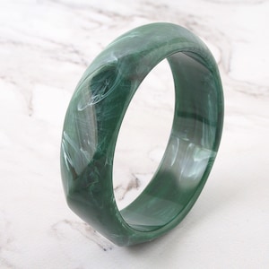 May include: A green and white marbled bangle bracelet. The bangle is made of a smooth, glossy material and has a slightly rounded shape.