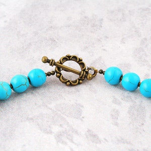 Op de afbeelding: Een turquoise kralenketting met een bronzen sluiting. De kralen zijn rond en hebben een licht onregelmatige vorm.