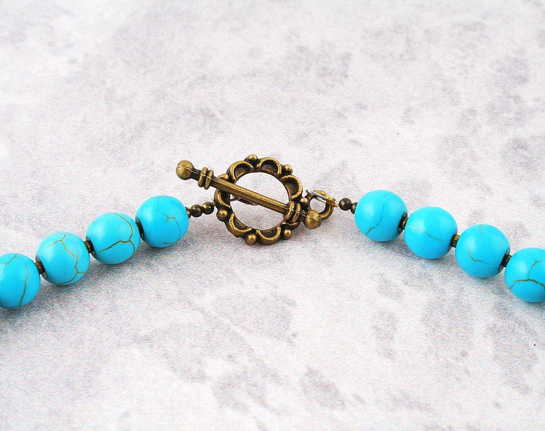 Op de afbeelding: Een turquoise kralenketting met een bronzen sluiting. De kralen zijn rond en hebben een licht onregelmatige vorm.