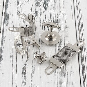 May include: A set of five silver cufflinks with different designs. One cufflink features a mesh design, another has a crystal, and another has a simple bar design. The remaining two cufflinks have a more ornate design.