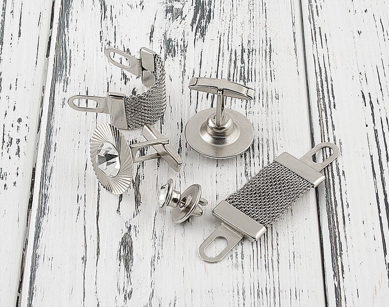 May include: A set of five silver cufflinks with different designs. One cufflink features a mesh design, another has a crystal, and another has a simple bar design. The remaining two cufflinks have a more ornate design.