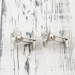 May include: A pair of silver cufflinks with clear crystal accents. The cufflinks have a simple, elegant design.