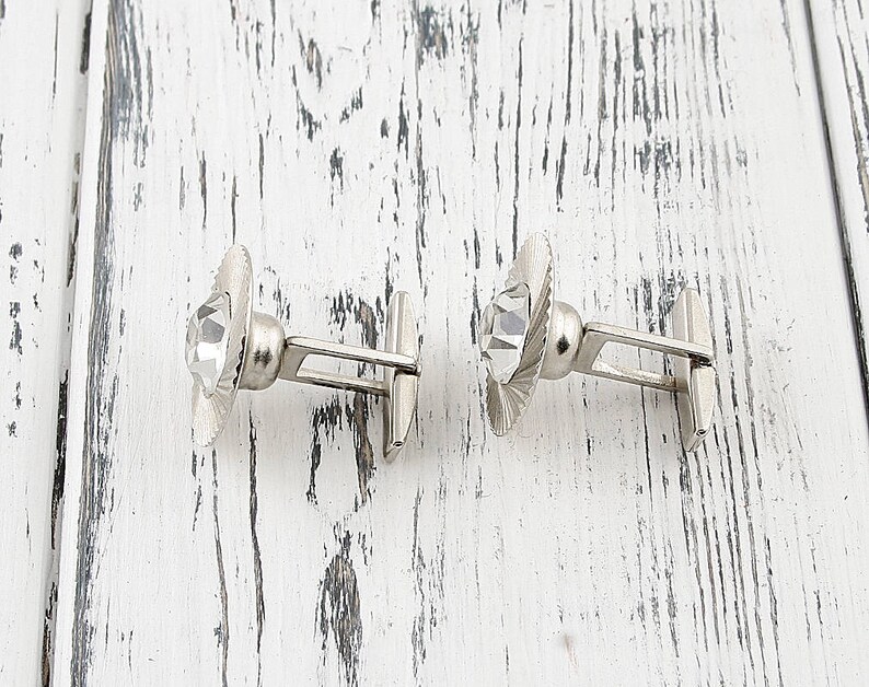 May include: A pair of silver cufflinks with clear crystal accents. The cufflinks have a simple, elegant design.