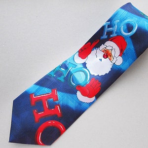 Op de afbeelding: Een blauwe en rode kerstdas met een kerstmanontwerp en de woorden "HO HO HO" erop gedrukt.