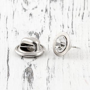 May include: Two silver-toned metal hat-shaped pin backs with a clear rhinestone in the center. The pin backs are used to attach a pin to a garment.