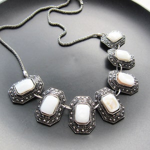 May include: A silver necklace with a chain and six white oval-shaped stones set in ornate silver frames.