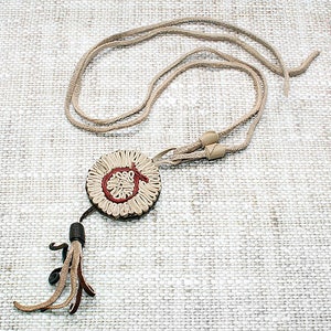 May include: A beige leather necklace with a round, cream and red leather pendant and a tassel.