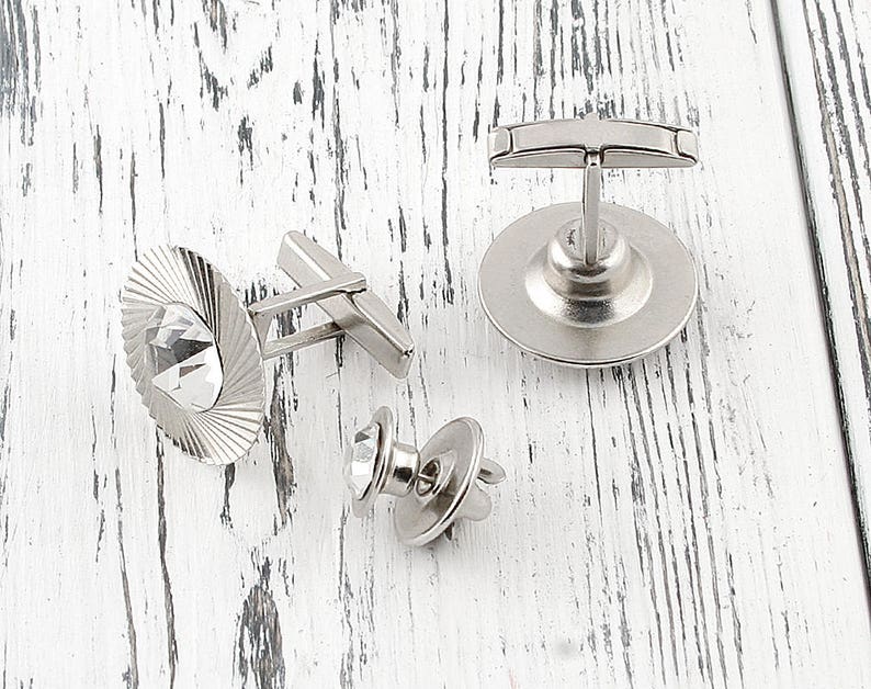 May include: Three silver cufflinks with clear crystal accents. One cufflink features a round design with a crystal in the center. Another cufflink features a rectangular design with a crystal in the center. The third cufflink features a round design with a crystal in the center.