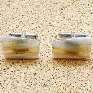 Puede incluir: Un par de gemelos con un diseño de piedra de ágata blanca y marrón. Los gemelos tienen una base de metal plateado.