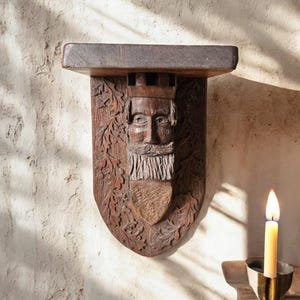 May include: A wooden wall sculpture of a bearded man's face with a crown, carved with oak leaves and a shield. The sculpture is mounted on a wooden shelf.
