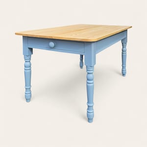 May include: A rectangular wooden table with a light blue base and a natural wood top. The table has a single drawer with a round knob and turned legs. The table measures approximately 122 cm long, 76 cm wide, and 76 cm high.