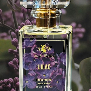 May include: A clear glass perfume bottle with a faceted crystal top and gold accents. The label features the text "Air & Weather" and "LILAC" with a purple floral design. The bottle contains 30 ml of perfume.
