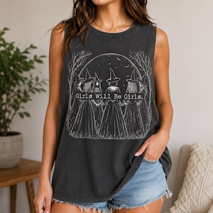 Könnte beinhalten: Ein ärmelloses Tanktop in Anthrazit mit einem weißen Grafikdruck von fünf Figuren mit spitzen Hüten, die in einem Kreis unter einem großen Mond und kahlen Bäumen stehen. Der Text Girls Will Be Girls ist in Weiß mittig auf das Design gedruckt.