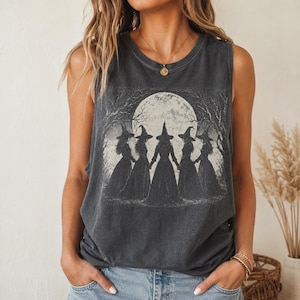 Könnte beinhalten: Ein ärmelloses Tanktop in Anthrazit mit einem Grafikdruck von fünf Gestalten in spitzen Hüten und langen Kleidern, die unter einem großen Vollmond und kahlen Bäumen in einem Kreis stehen. Das Kleidungsstück hat einen Rundhalsausschnitt.