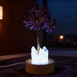 Pode incluir: Uma lâmpada decorativa de árvore de cristal de ametista. A árvore apresenta um tronco e galhos cor de cobre adornados com cristais roxos. A base é um disco de madeira com cristais transparentes iluminados.