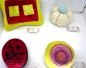May include: A collection of four handmade felt items. Includes a yellow pillow with red and green accents, a white flower-shaped item with a blue center, a red ladybug, and a yellow spiral design with pink and orange hues. Each item is unique.