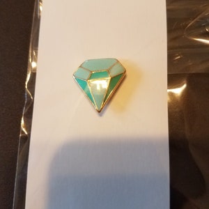 May include: A gold-toned diamond-shaped pin with a light blue and green enamel design.