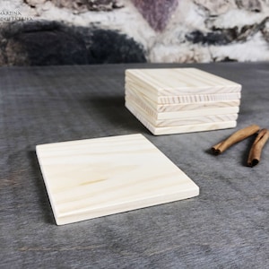 Può includere: Una pila di sei sottobicchieri in legno grezzo, con un sottobicchiere piatto su una superficie grigia. I sottobicchieri sono in legno chiaro con una venatura naturale. Due bastoncini di cannella sono appoggiati sulla superficie accanto al sottobicchiere.