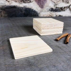 Può includere: Una pila di sei sottobicchieri in legno grezzo, con un sottobicchiere appoggiato su una superficie grigia. I sottobicchieri sono in legno chiaro con una venatura naturale. Due bastoncini di cannella sono appoggiati sulla superficie accanto al sottobicchiere.