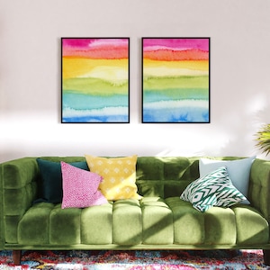 May include: Two framed watercolour paintings with a rainbow colour scheme. The paintings are hung on a white wall above a green velvet sofa with colourful throw pillows.