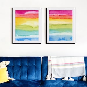 May include: Two framed abstract watercolour paintings with horizontal stripes of pink, orange, yellow, green, blue, and light blue.