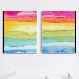 May include: Two framed abstract watercolour paintings with horizontal stripes of pink, orange, yellow, green, blue, and light blue.