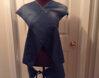 May include: A denim vest made from recycled jeans, displayed on a mannequin. The vest features a wrap-around design with a V-neck and tie closure at the waist. The blue denim shows signs of wear.
