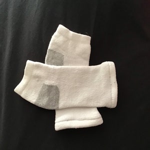 May include: Two white ankle socks with gray heels and toes are arranged on a black surface. The socks are made of a soft, textured material.