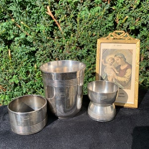 May include: A set of three silver-plated cups, each engraved with the initials "PP". The cups are of varying sizes and shapes, including a tall cup, a small cup, and a ring-shaped cup. A small framed picture of a religious image is also included in the image.
