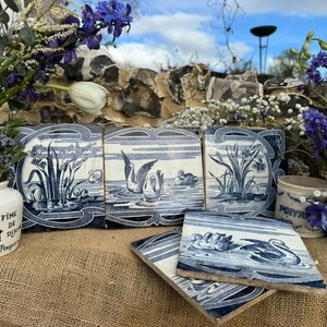 May include: A display of blue and white ceramic tiles and decorative jars. The tiles depict swans and aquatic plants. A small jar with a crown emblem and text is on the left. A jar with the word "POIVRE" is on the right.
