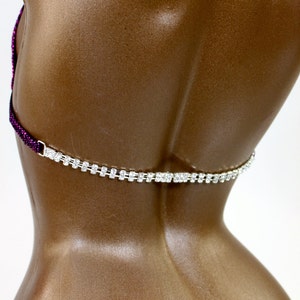May include: A close-up of a brown mannequin torso with a rhinestone-studded silver chain. The top of the garment is a dark purple beaded design. The chain is a delicate, sparkling accent.
