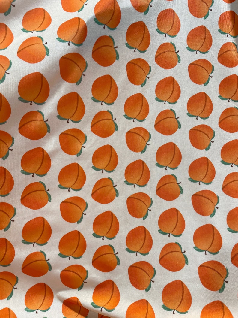 May include: A white fabric with a repeating pattern of orange peaches. The peaches have green leaves.