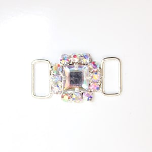 May include: Silver metal buckle with a square-shaped rhinestone embellishment. The rhinestones are iridescent and have a rainbow effect.