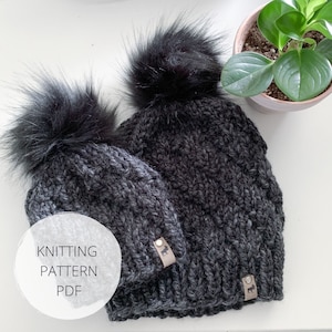 May include: Two black knit hats with black pom poms. The hats have a textured knit pattern and are labeled with a small brown leather tag. The text "Knitting Pattern PDF" is written in white on a white circle.