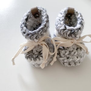 May include: A pair of grey and white crocheted baby booties with white leather ties.