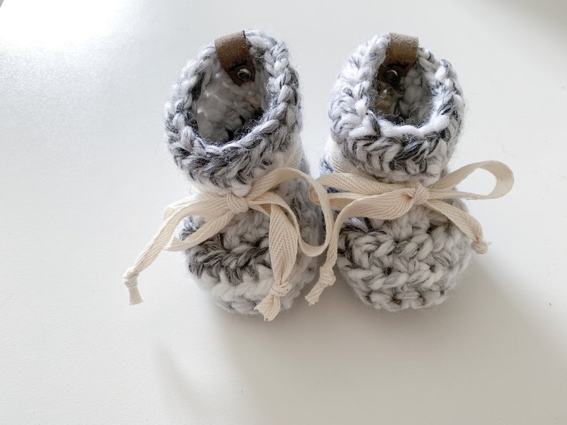 May include: A pair of grey and white crocheted baby booties with white leather ties.