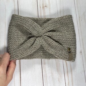 Peut inclure: Un bandeau en tricot gris avec un design nou&eacute; et une petite &eacute;tiquette en cuir marron avec un logo.