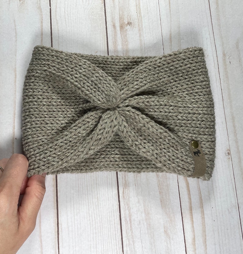 Peut inclure: Un bandeau en tricot gris avec un design nou&eacute; et une petite &eacute;tiquette en cuir marron avec un logo.