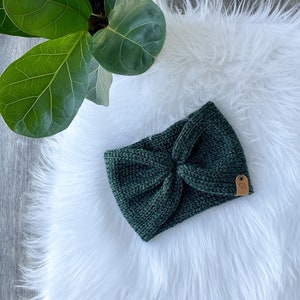 Peut inclure: Un bandeau en tricot vert fonc&eacute; avec un n&oelig;ud en forme de n&oelig;ud. Le bandeau a une petite &eacute;tiquette en cuir marron avec le texte "Made with Love" dessus.