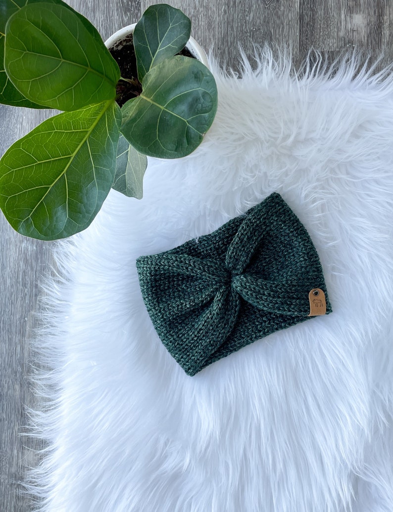 Peut inclure: Un bandeau en tricot vert fonc&eacute; avec un n&oelig;ud en forme de n&oelig;ud. Le bandeau a une petite &eacute;tiquette en cuir marron avec le texte "Made with Love" dessus.