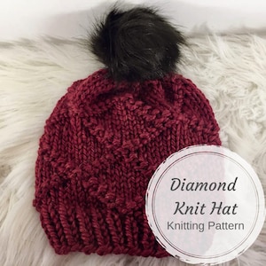May include: A burgundy knit hat with a black pom pom. The hat has a diamond pattern and the text "Diamond Knit Hat Knitting Pattern" is written on a white circle.